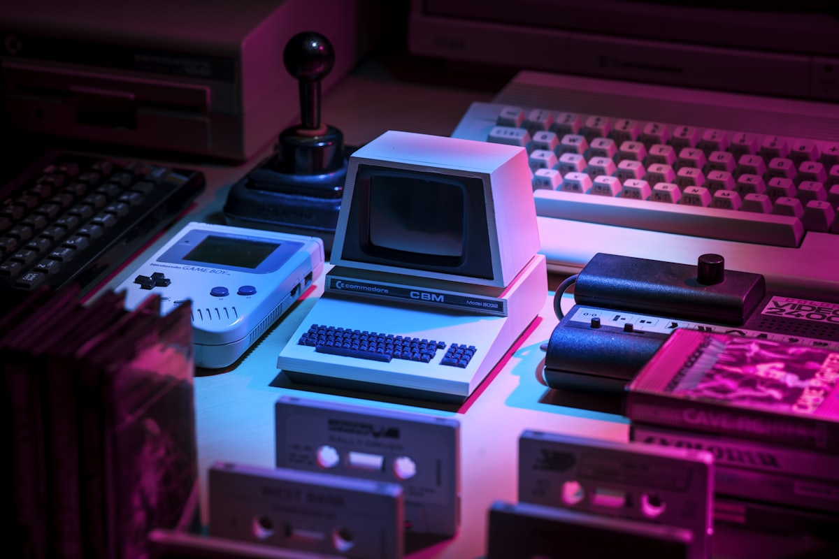 A neon-lit desk of retro handhelds, cassettes and a joystick